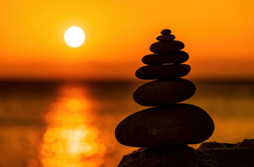 Balanced pebble pyramid silhouette on the beach on sunset.