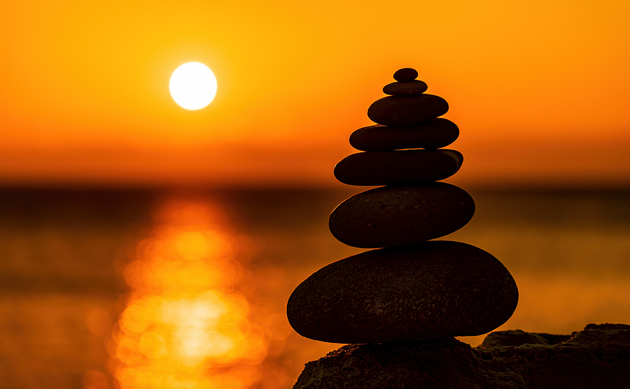 Balanced pebble pyramid silhouette on the beach on sunset.